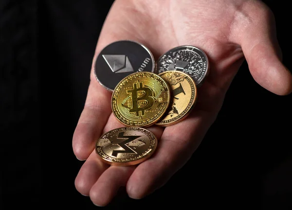 Bitcoin and other dofferent crypto currency coins in male hand palm over black background, close up — Stockfoto