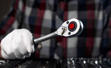Metal tool, socket ratchet handle, in male hand of repairman in checkered shirt, close up