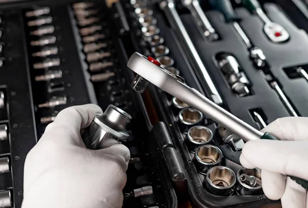Hands of repairman in gloves close up with metal steel socket ratchet handle over toolbox, POV