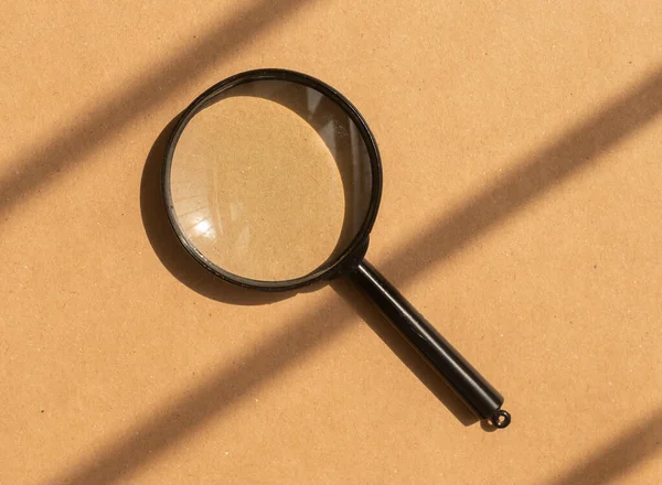 Magnifying glass over brown carton background with day light and shadows. Search tool — Stock Photo, Image