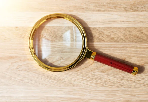 Golden magnifying glass on wood desk. Magnifier on wooden background — Stock Photo, Image