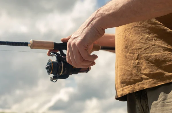 Manos de pescador sosteniendo caña de carrete giratorio o cebo cuchara y la pesca de cerca. Cielo de verano con nubes en el fondo — Foto de Stock