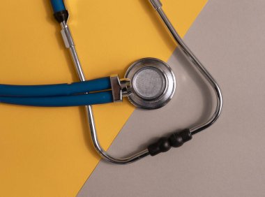 Tıbbi araç, gri ve sarı arka planda mavi steteskop, üst görünüm.