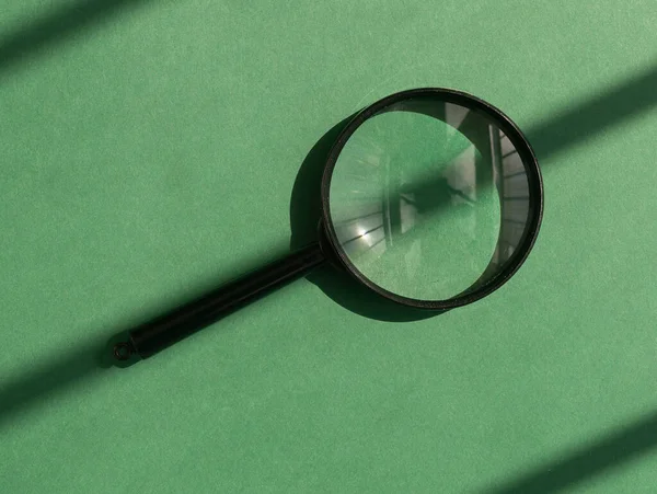 Magnifying lens over green background with sunlight and shadow stripes. Magnifier concept — Stock Photo, Image