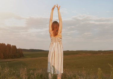 Elleri havada bir kadın yaz tarlasında özgürlüğün ve manzaranın tadını çıkarıyor. Kendinle uyum içinde özgür olmanın zevki.