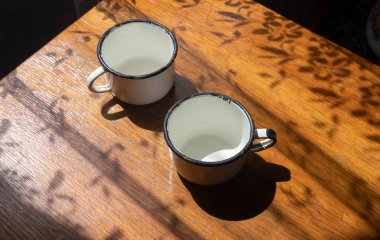 Günah aydınlığı ve gölgeli, eski ahşap masanın üzerinde su olan iki metal beyaz bardak.