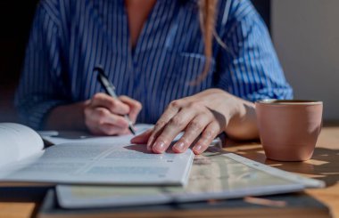 Öğrenci ellerindeyse not defterinde kalemle yakın çekim yazıları, kitaptan notlar almak, kafede kahve fincanıyla ders çalışmak.