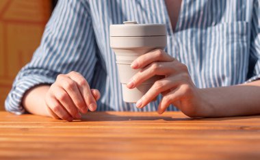 Kadın elleri, yeniden kullanılabilir silikon, ekolojik kahve fincanını ahşap masanın üzerinde tutuyor.