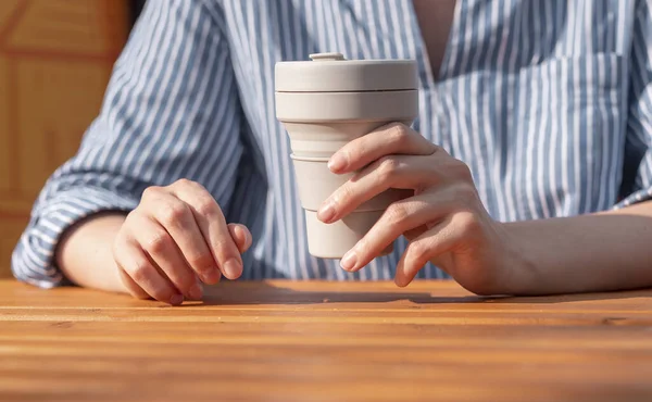 Kobieta ręce zbliżenie gospodarstwa wielokrotnego użytku krzemu na wynos kubek eko kawy w rękach nad drewnianym stole — Zdjęcie stockowe