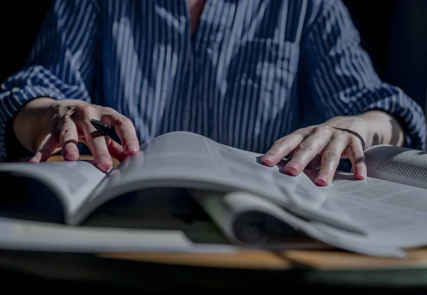 Student hands closeup holding pen and reading many books. Concept of research and searching answers in textbooks and academic literature