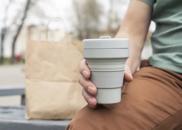 Collapsible cup for takeaway coffee or tea. Male hand with sustainable silicon mug. Eco-friendly lifestyle of man in city — Zdjęcie stockowe