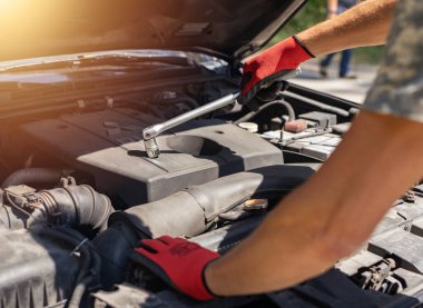 Eldivenli bir adam ingiliz anahtarıyla arabayı tamir ediyor ve kaputu açıyor.