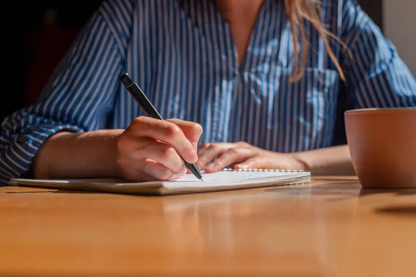 Mulheres mão com planos de escrita caneta no planejador ou tomar notas sobre caderno sobre mesa de madeira, close-up — Fotografia de Stock