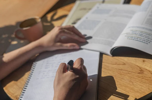 Mãos femininas escrevendo com caneta em caderno ou planejador, tomando notas, estudando com livro didático, close-up — Fotografia de Stock