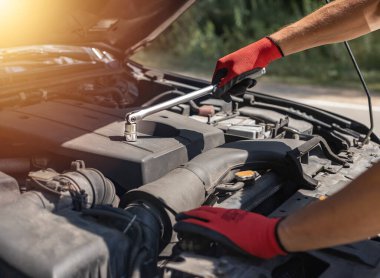 Araba tamircisi, yolda ingiliz anahtarı ve kapüşonuyla otomobil motoru tamir ediyor.