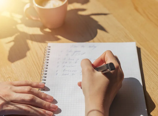 Mulheres mão escrever planos em notebook ou planejador sobre mesa de café de madeira com luz solar da janela — Fotografia de Stock