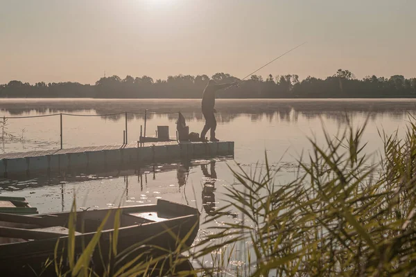 Ψαράς που ψαρεύει σε ομιχλώδες πρωινό. Άνδρας σιλουέτα αναπαύεται με ράβδο στο ποτάμι ή στη λίμνη στην ομίχλη — Φωτογραφία Αρχείου