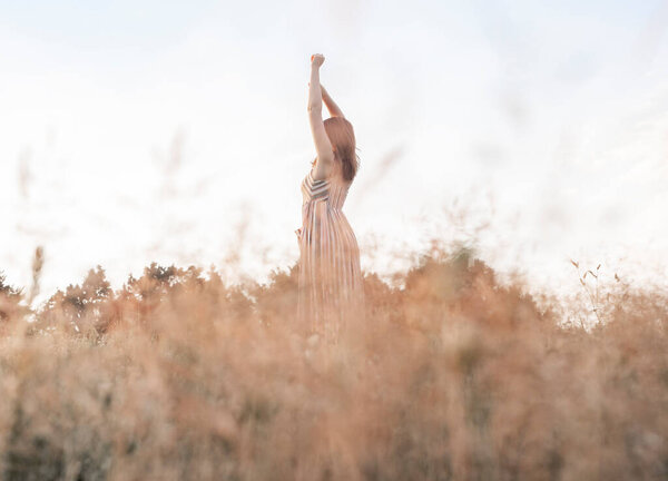 Woman with hands up in summer field enjoying freedom and landscape.