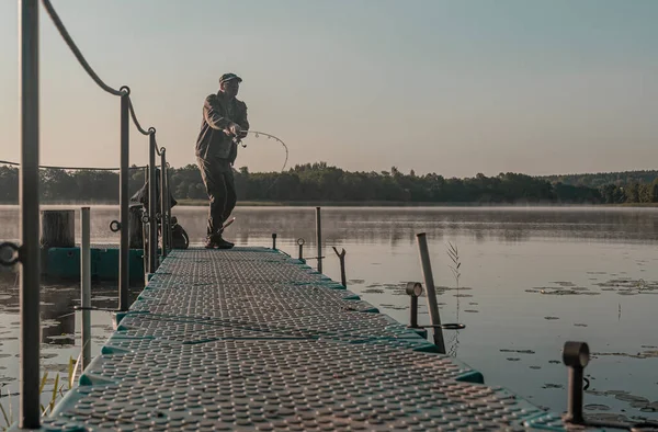 Pescatore pesca nella nebbia la mattina presto. Uomo con asta di pesce volante appoggiato sul fiume all'alba — Foto Stock
