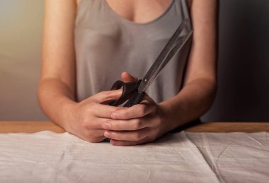 Profesyonel terzi elleriyle terzi makası tutuyor. Doğal pastel kumaşın üzerine yakın plan.