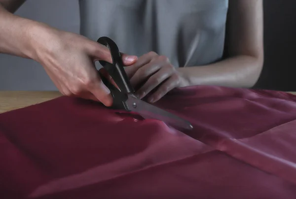 Vrouwen handen snijden glanzende rode stof met naaischaar. Kleermaker aan het werk — Stockfoto