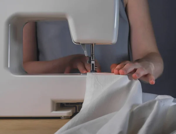 Manos de costurera con tela de lino en la máquina de coser, proceso de trabajo con textil orgánico de algodón natural — Foto de Stock