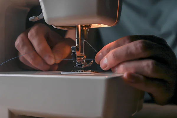 Manos masculinas insertando hilo a través del orificio de la aguja en la máquina de coser, comenzando su trabajo —  Fotos de Stock