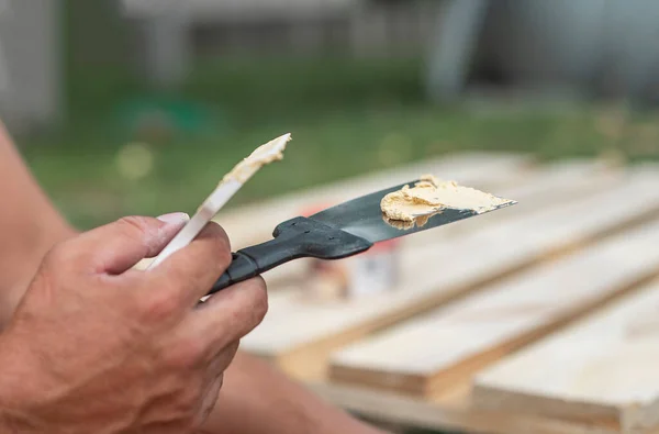 Erkeklerin elindeki spatula aletinde macun, ahşabı yapıştırıcıyla tamir ediyor.