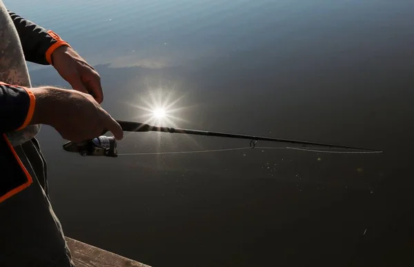 Αρσενικά χέρια που κρατούν καλάμι ψαρέματος κοντά πάνω από ποτάμι ή λίμνη με αντανάκλαση των ακτίνων του ήλιου — Φωτογραφία Αρχείου