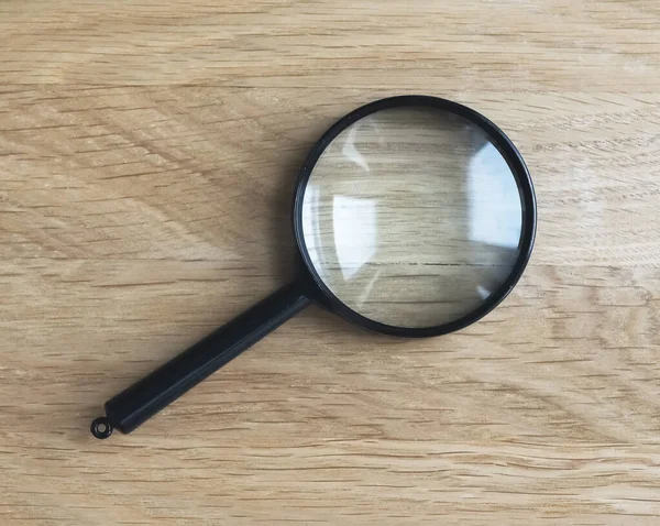 Magnifying lens on wood desk as symbol of research — Stock Photo, Image