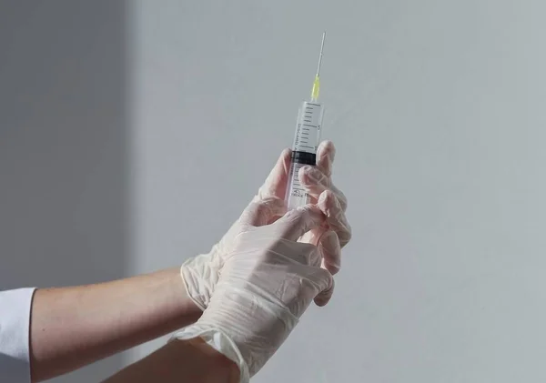 Jeringa con aguja en manos de enfermero con guantes blancos sobre fondo con luz diurna y sombra — Foto de Stock
