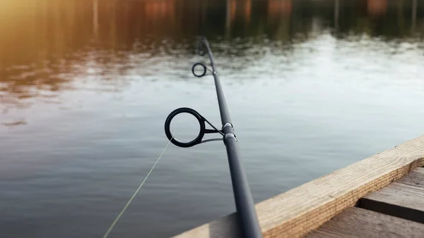 Caña de pescar sobre el agua del lago, acostado en el embarcadero de madera — Foto de Stock