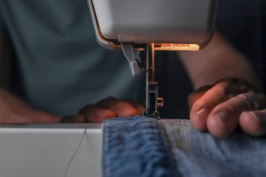 Dikiş makinesinde kot kumaşlarıyla çalışan bir adam. Moda tasarımcısı