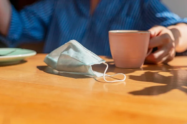 Xícara de café e máscara facial na mesa de madeira no café. Novo conceito normal — Fotografia de Stock