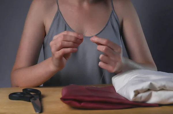 Hands inserting thread through needle hole for sewing at her wood desk — Stock Photo, Image