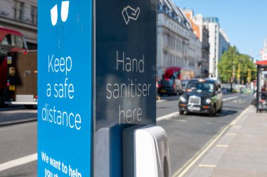 Londra, İngiltere - 1 Haziran 2021: El dezenfektan istasyonlu bir caddede insanlardan arka planda taksiyle güvenli bir mesafede durmalarını isteyen bir tabela