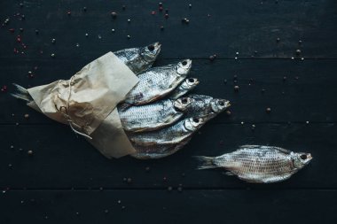 Parşömen kağıdına sarılı lezzetli gümüş koç balığı. Koyu ahşap masa üzerinde bir iple sarılmış ve farklı baharat çeşitleri olan bir balık buketi. Bir balık yanında.