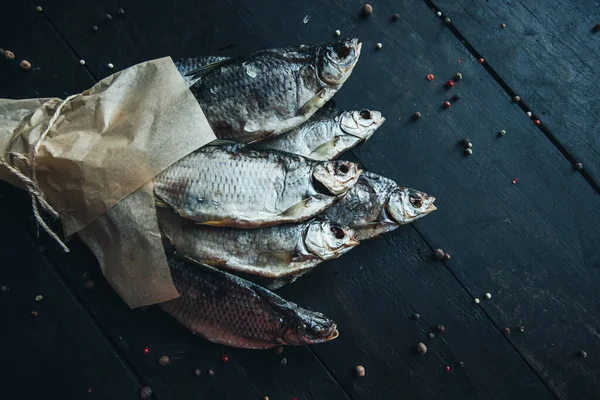 delicious dried silver ram fish wrapped in paper in parchment paper for cooking wrapped with a rope on the dark wooden table with different kinds of spices bouquet of fish