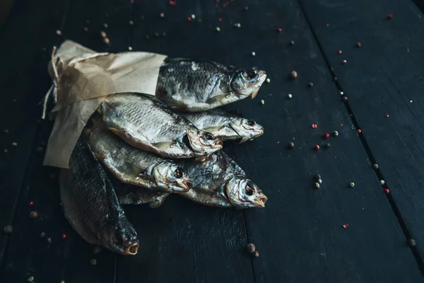 delicious dried silver ram fish wrapped in paper in parchment paper for cooking wrapped with a rope on the dark wooden table with different kinds of spices bouquet of fish