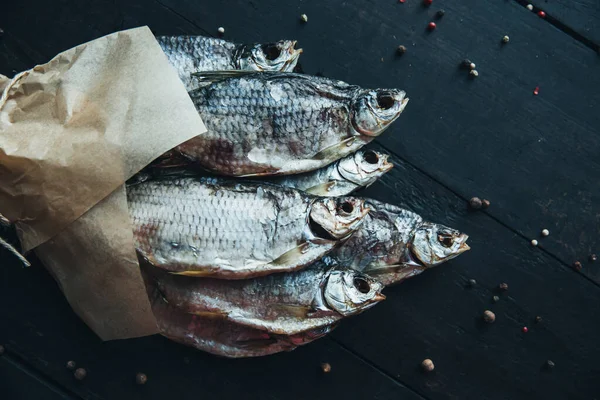 delicious dried silver ram fish wrapped in paper in parchment paper for cooking wrapped with a rope on the dark wooden table with different kinds of spices bouquet of fish