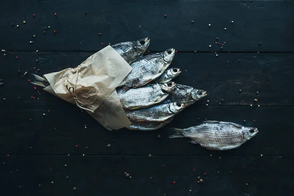 delicious dried silver ram fish wrapped in paper in parchment paper for cooking wrapped with a rope on the dark wooden table with different kinds of spices bouquet of fish one fish near