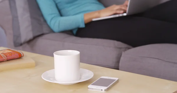 Mug sitting on table in front of woman working on laptop — Stock Photo, Image