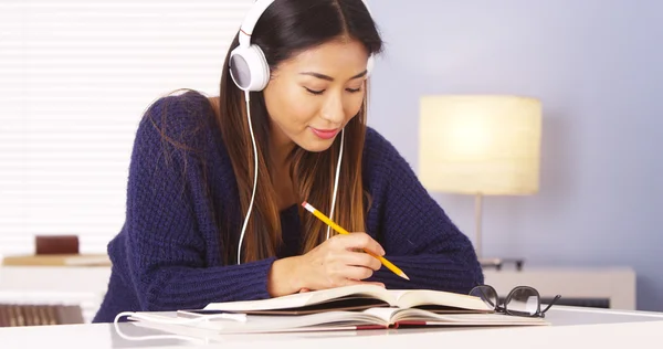 Asiatin hört Musik, während sie Hausaufgaben macht — Stockfoto