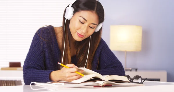 Asian woman listening to music while doing homework — Stock Photo, Image
