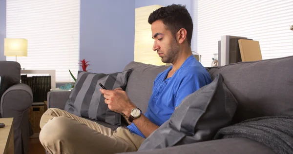 Mexican man smiling and texting on couch — Stock Photo, Image