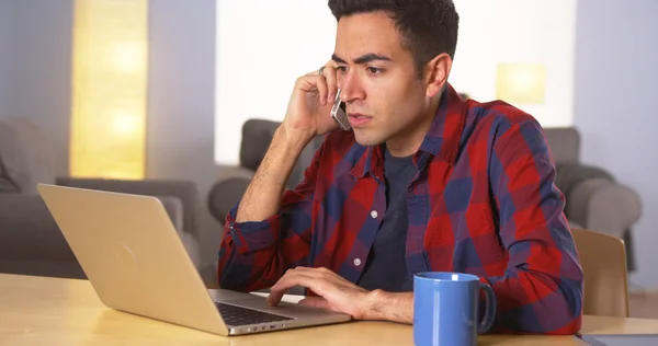 Mexicaanse man gebruikend smartphone en die op laptop werkt — Stockfoto