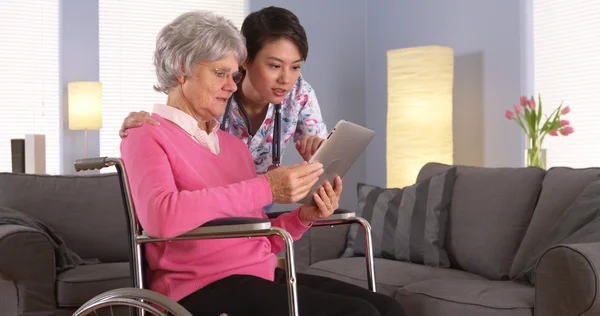 Ältere Patientin und asiatische Krankenschwester im Gespräch mit Tablet — Stockfoto