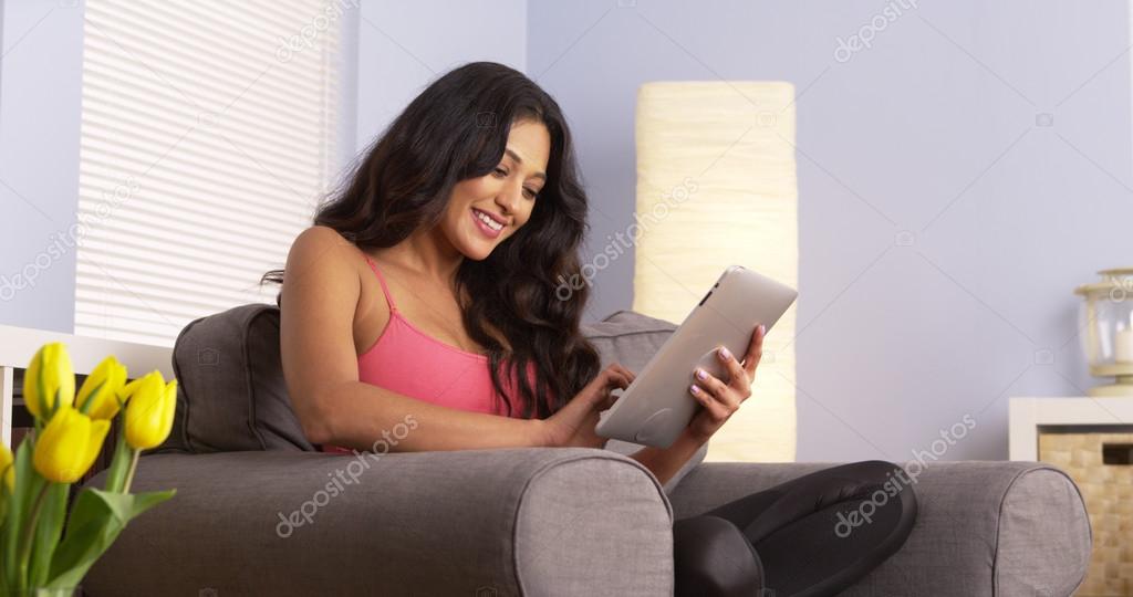 Cute Mexican woman using tablet on couch