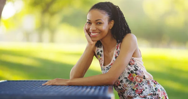 Musta nainen istuu puistossa penkillä hymyillen — kuvapankkivalokuva