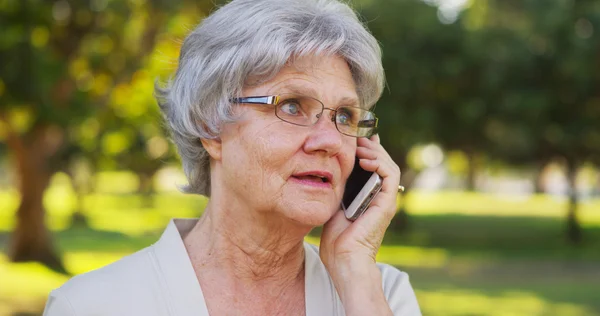 Äldre kvinna talar på smartphone på park — Stockfoto